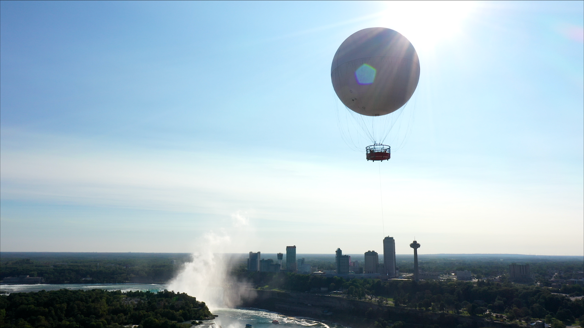 Balloon over cityscape with waterfall and mist under a bright sun.